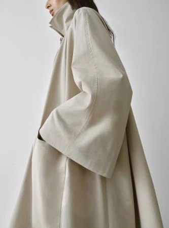Model Nora Attal wearing an oversized cream trench coat against a white background for Nour Hammour Spring Summer 26.