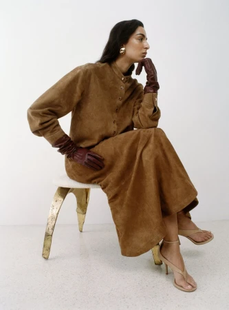 Model Nora Attal seated on a stool in a brown buttoned dress and burgundy leather gloves for Nour Hammour Spring Summer 26