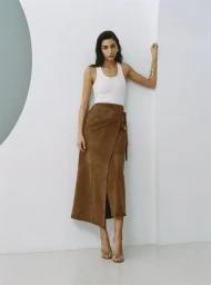 Model Nora Attal wearing a white tank top and brown skirt against a white studio wall