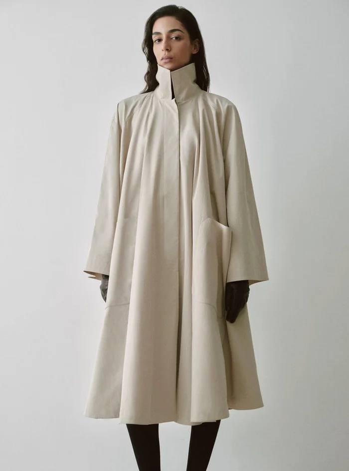 Model Nora Attal in a high-necked cream coat for Nour Hammour Spring Summer 26 against a white background