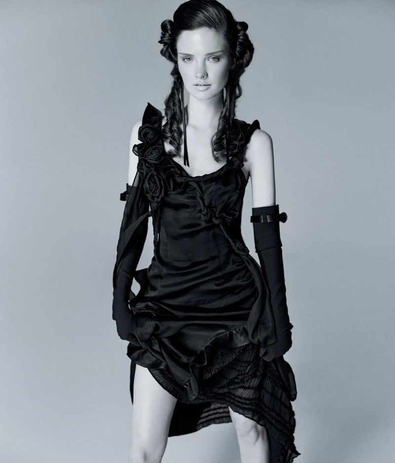 Model in a black dress with floral appliqués and long black gloves against a grey seamless background