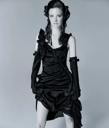 Model in a black dress with floral appliqués and long black gloves against a grey seamless background