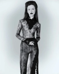 Model in sheer black lace bodysuit and dark lipstick standing against a plain light background for Elle Lithuania editorial