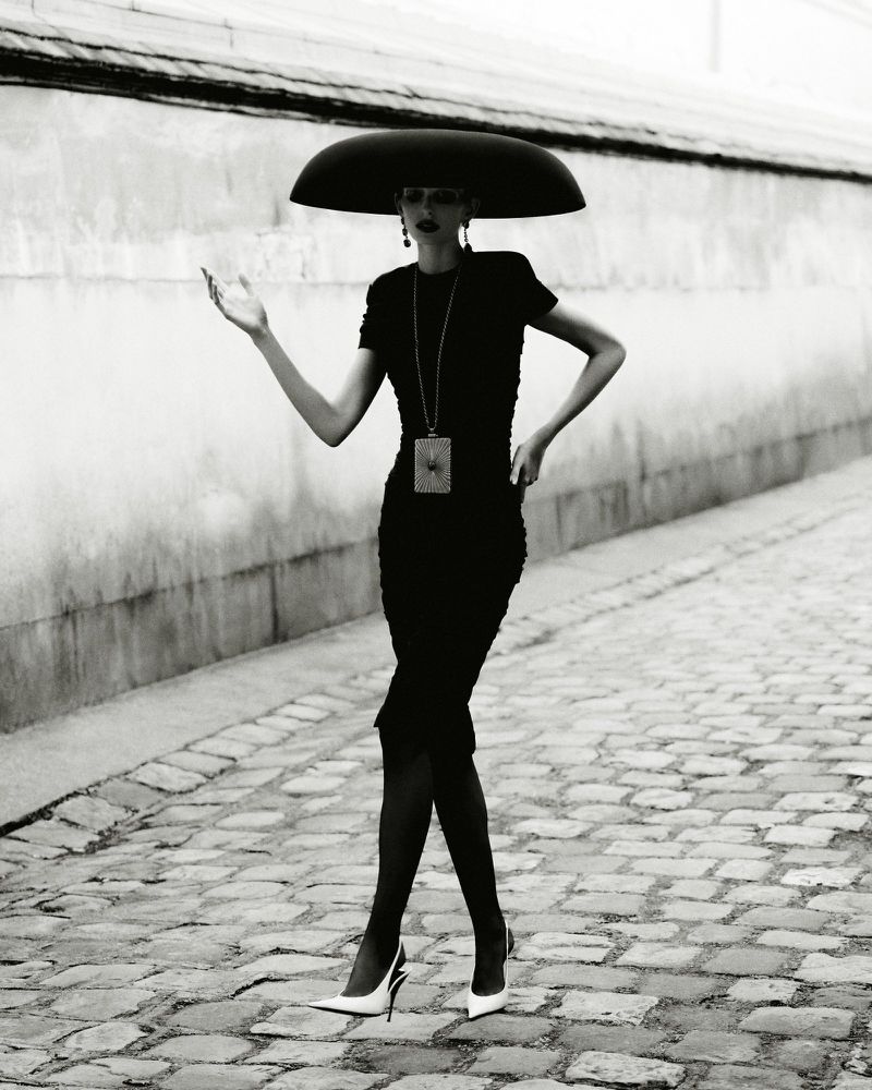 Model in wide black hat and black dress walking on cobblestone street photographed by Robin Galiegue for Beyond Noise