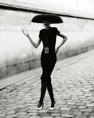 Model in wide black hat and black dress walking on cobblestone street photographed by Robin Galiegue for Beyond Noise