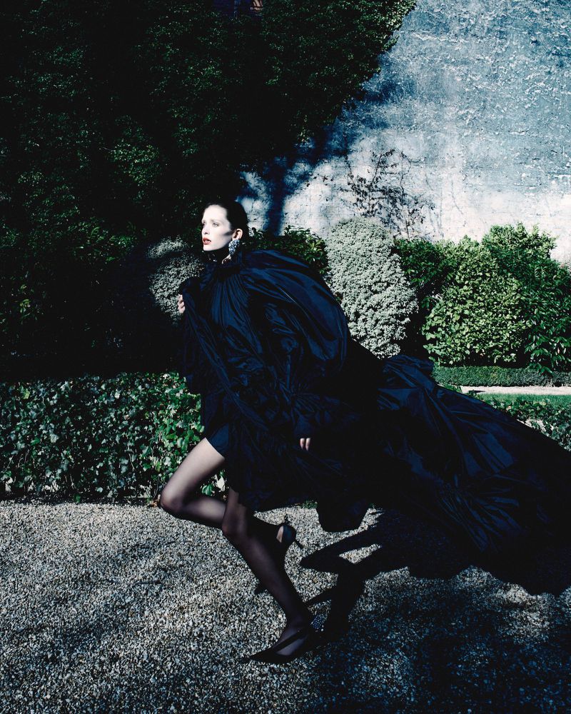 Model in a voluminous black dress running across a gravel path in a garden for Beyond Noise Issue 5