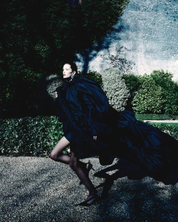 Model in a voluminous black dress running across a gravel path in a garden for Beyond Noise Issue 5
