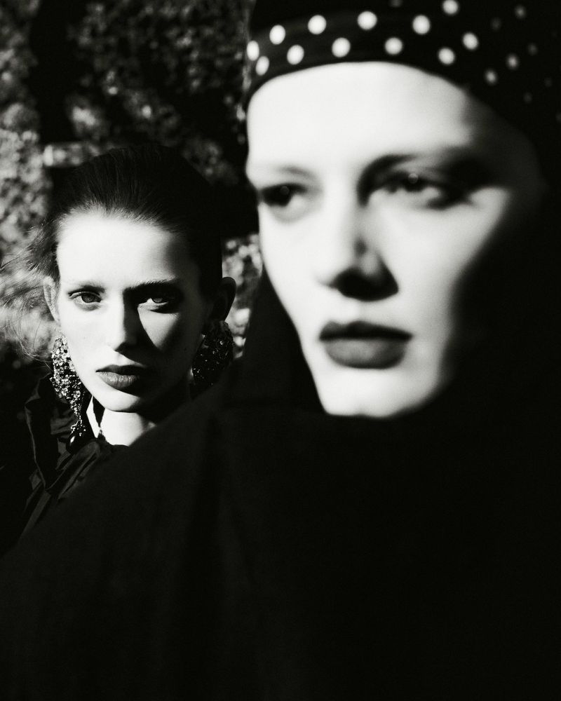 Two women posing in a high contrast black and white fashion portrait with one wearing a polka dot headscarf