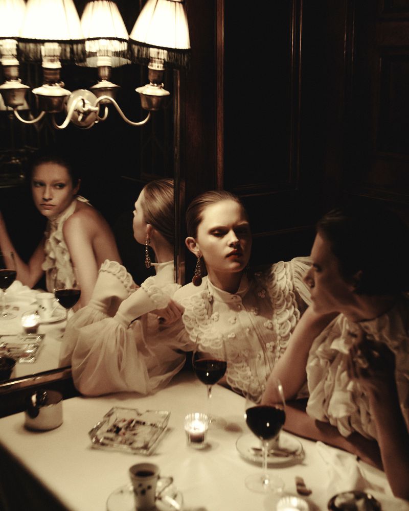 Group of women seated at a table with wine glasses and lit candles reflecting in a mirror under vintage lamps in Beyond Noise issue 5.