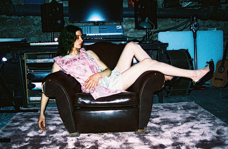 Woman in a pink patterned dress lounging in a leather armchair inside a recording studio with audio equipment