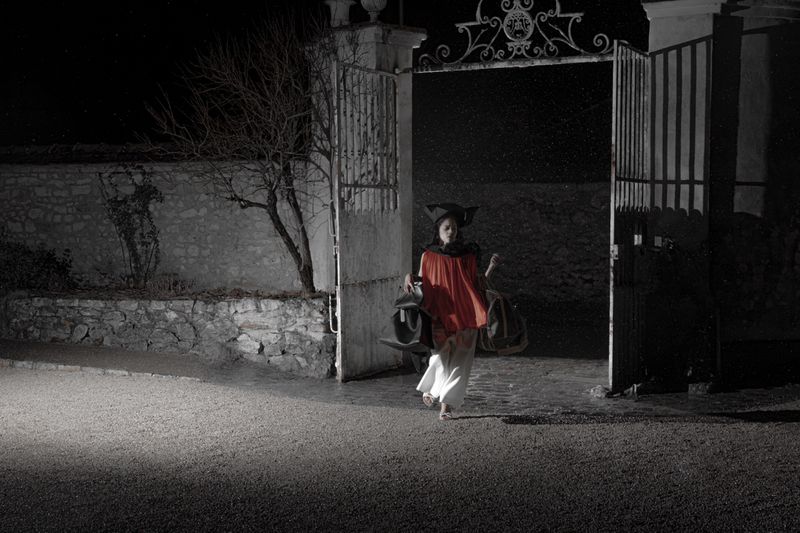 Model carrying bags and walking through tall iron gates at night under harsh lighting for Dazed MENA I'TIMAD