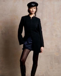 Model in black coat and matching cap wearing lace-up boots against a textured background