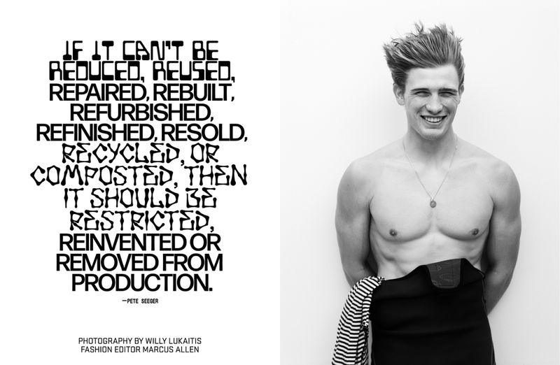 Black and white portrait of a smiling male model wearing a wetsuit pulled down, standing against a plain white background.