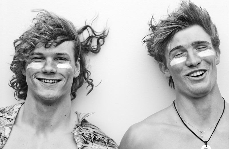 Black and white portrait of two smiling young male models with zinc cream on their cheeks against a plain background