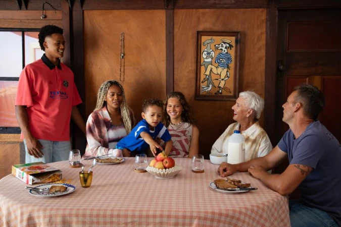 Multigenerational family gathered around a round table set with food in a wood-paneled room for Pop Magazine