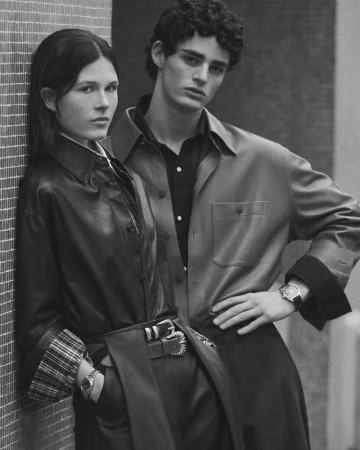 Black and white portrait of a woman leaning against a tiled wall and a man standing next to her wearing buttoned shirts