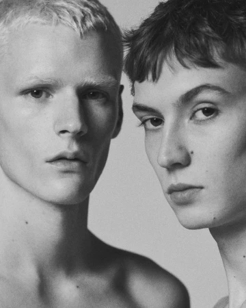 Close-up portrait of two young male models with distinct hairstyles against a neutral studio backdrop.