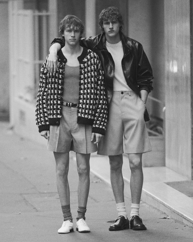 Two young male models posing together on a city street for Behind the Blinds magazine editorial.