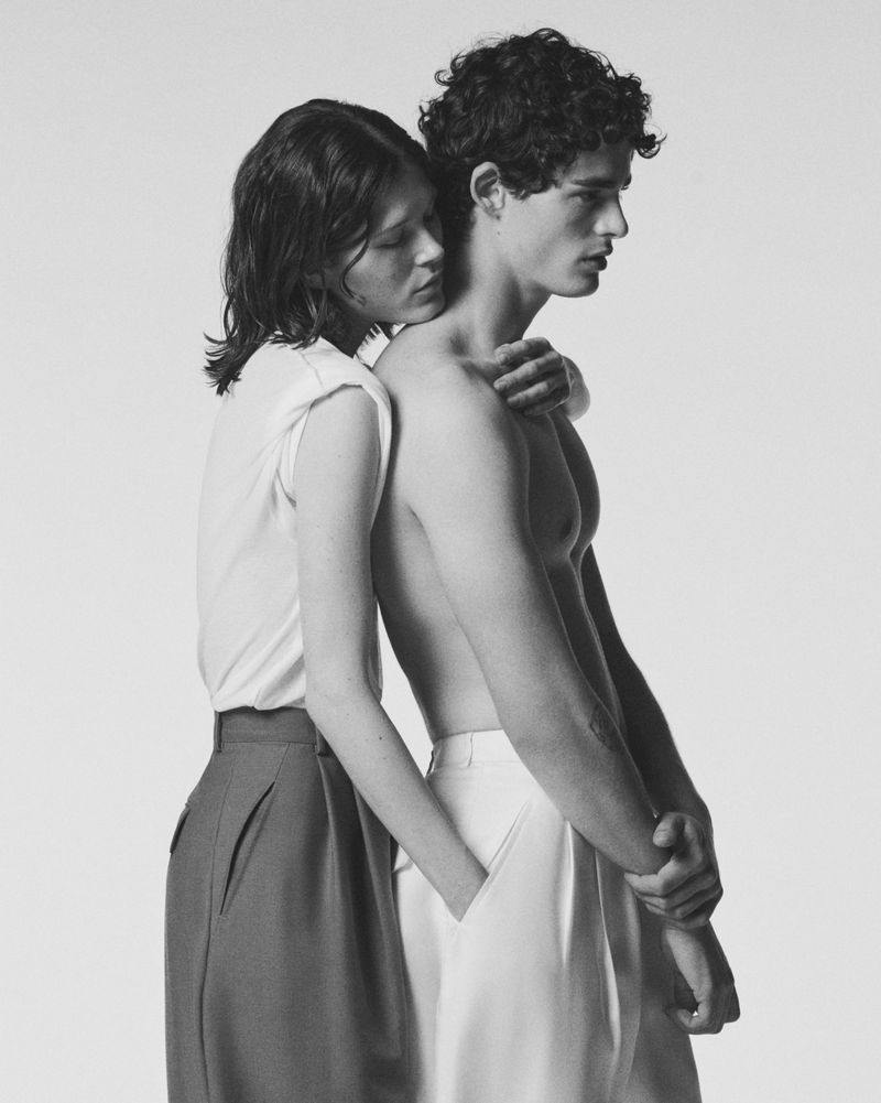 Two models embracing against a seamless white background in a black and white fashion portrait.