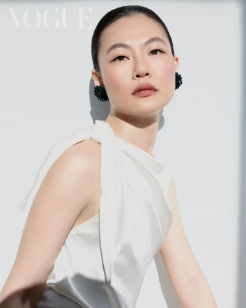 Asian woman in a white silk top with dark earrings posing against a plain white background for Vogue Taiwan.