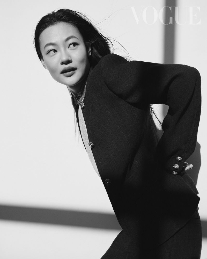 Black and white portrait of a woman wearing a black blazer against a white background with hard lighting and the VOGUE magazine logo.