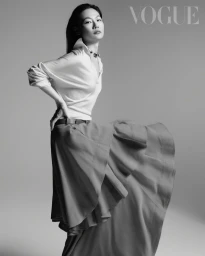 Model in white collared shirt and layered skirt posing against a seamless grey studio backdrop for Vogue Taiwan