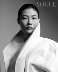 Portrait of a woman wearing a high-collared white coat against a seamless grey backdrop for Vogue Taiwan.