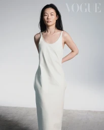 Woman with long dark hair wearing a sleeveless cream slip dress against a plain white studio background with Vogue text.