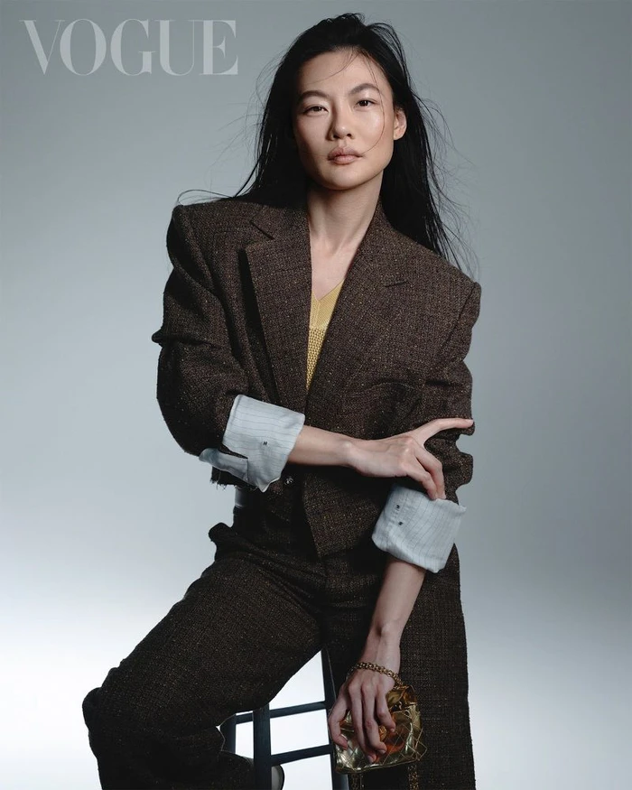 Zine Tseng wearing a brown tweed blazer and trousers for Vogue Taiwan, seated against a grey backdrop.