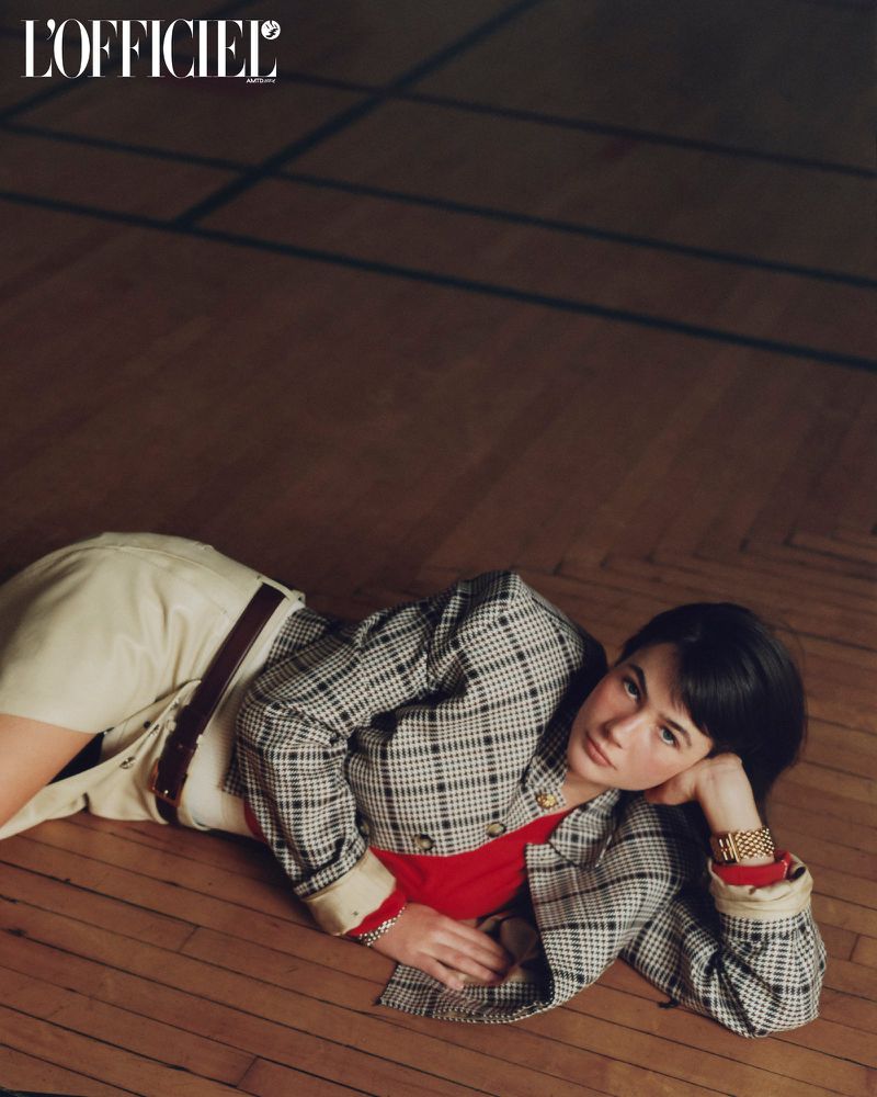 Model Grace Burns wearing a plaid jacket and red top lying on a dark wood parquet floor for L'Officiel USA.