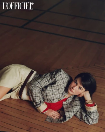 Model Grace Burns wearing a plaid jacket and red top lying on a dark wood parquet floor for L'Officiel USA.