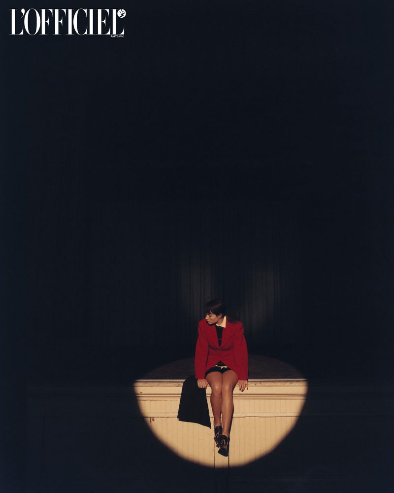 Model Grace Burns wearing a red jacket sitting in a spotlight for L'Officiel USA