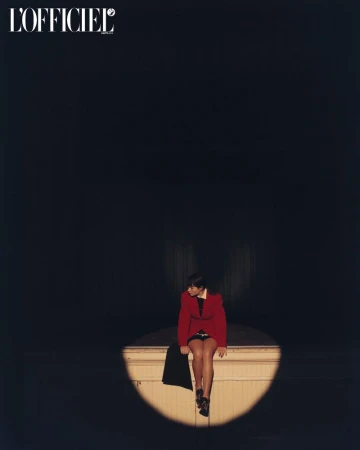 Model Grace Burns wearing a red jacket sitting in a spotlight for L'Officiel USA
