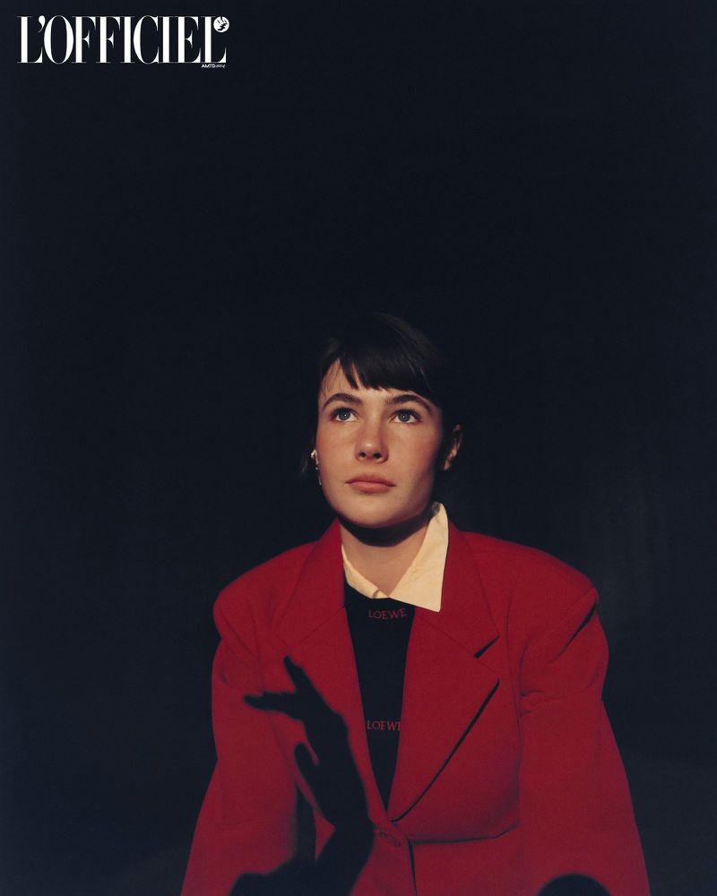 Model Grace Burns wearing a red blazer and black top against a dark background in an editorial portrait for L'Officiel USA.