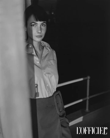 Black and white portrait of model Grace Burns wearing a buttoned shirt and skirt outdoors near a railing.