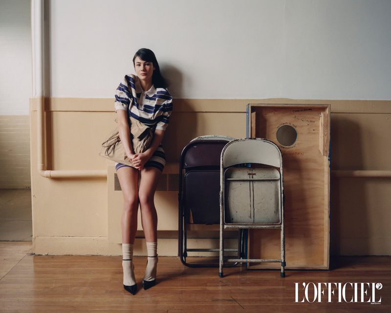 Model Grace Burns leaning against a wall wearing a striped dress and holding a bag for L'Officiel USA