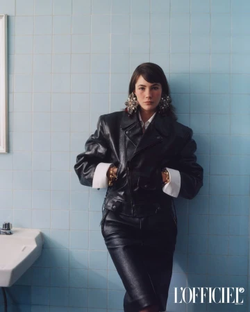 Model Grace Burns wearing a black leather jacket and skirt against a blue tiled wall for L'Officiel USA.
