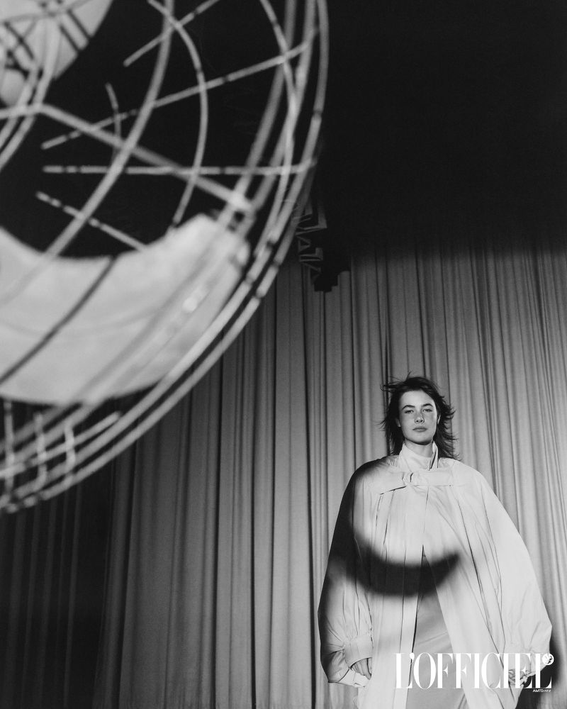 Monochrome fashion editorial image of Grace Burns standing before draped curtains with a large fan in the foreground