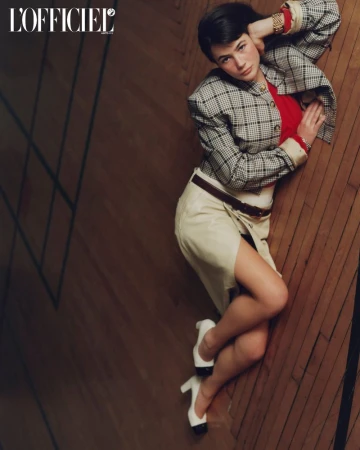 Model Grace Burns lying on a polished wooden floor wearing a plaid jacket and skirt for L'Officiel USA.