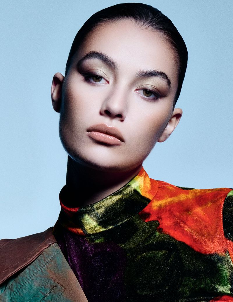Close-up portrait of a young adult female model with colorful velvet top against a light blue background in a photo studio.