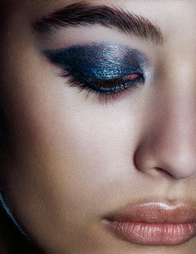 Close-up portrait of a woman wearing metallic blue eyeshadow and glossed lips for the L’entre Deux project by Schön! Switzerland