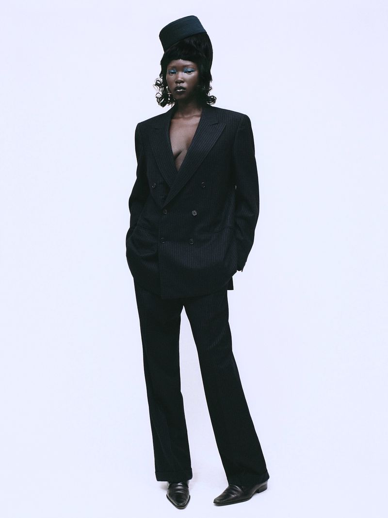 Black model wearing an oversized pinstripe suit and structured cap against a plain white background for Sicky Magazine.