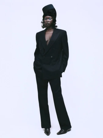 Black model wearing an oversized pinstripe suit and structured cap against a plain white background for Sicky Magazine.