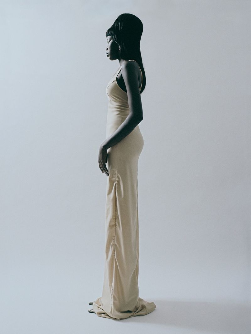 Model in a cream long slip dress standing in profile against a plain white studio background