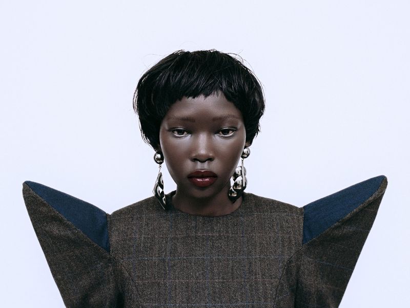 Portrait of a black woman wearing structured dark plaid top with exaggerated shoulders against a white background
