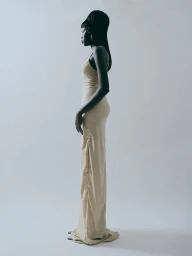 Model in a cream long slip dress standing in profile against a plain white studio background
