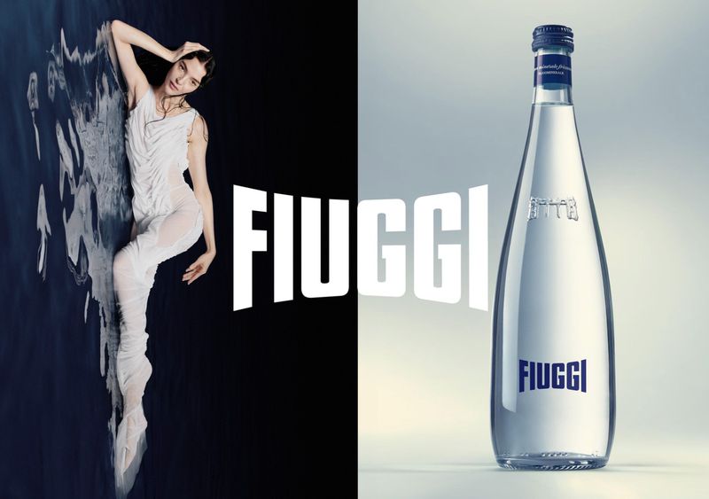 Model Mariacarla Boscono in a white dress next to a Fiuggi water bottle in an advertising campaign by Axel Morin.