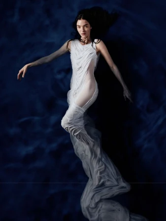 Mariacarla Boscono floating in water wearing a sheer white draped dress for the Mariacarla x Acqua FIUGGI campaign.
