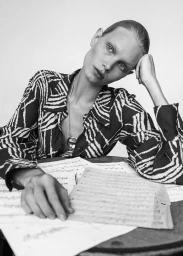 Monochrome portrait of a model in a patterned shirt leaning on a table with musical sheets for 5ELEVEN Magazine