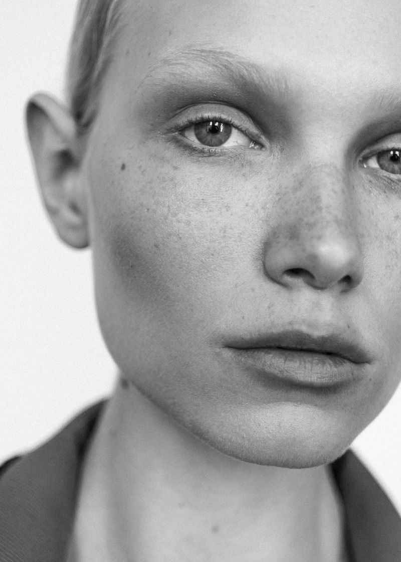 Close-up monochrome portrait of a model with light freckles and subtle makeup against a plain light background